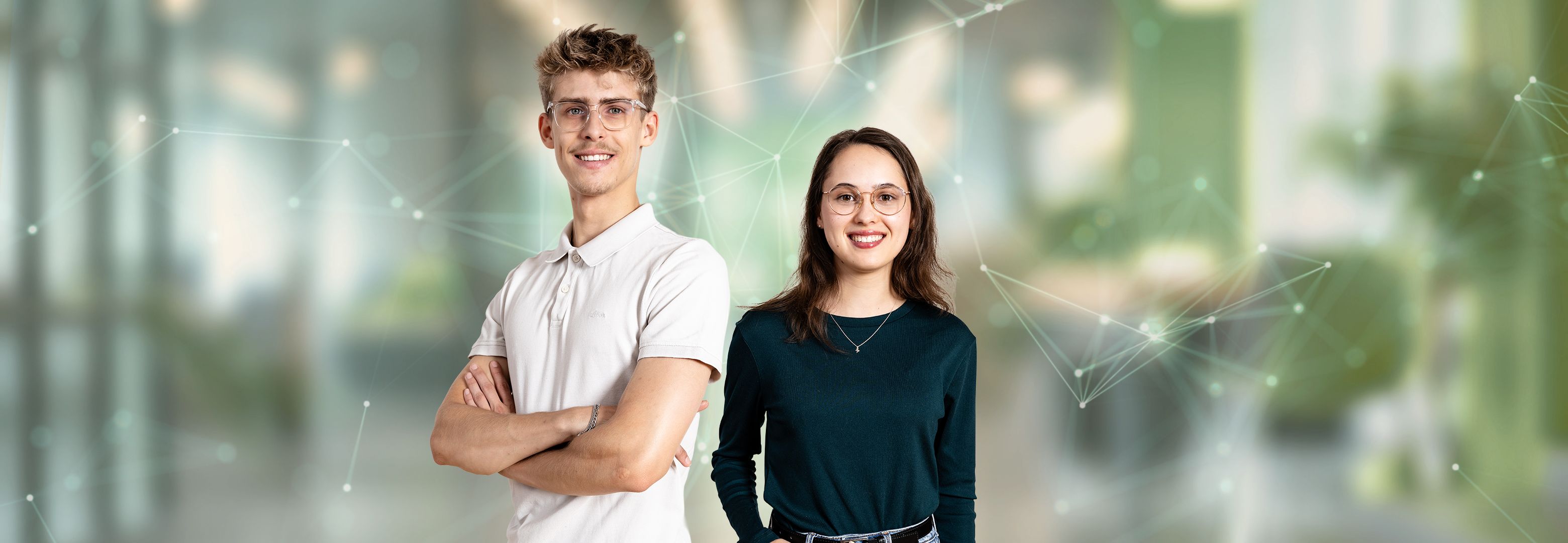 Ein Mann im weißen Poloshirt mit verschränkten Armen und eine Frau im dunkelgrünen Oberteil lächeln in die Kamera. Dahinter liegt ein unscharfer, grünlicher Hintergrund mit feinen Netzwerklinien und Lichtpunkten.